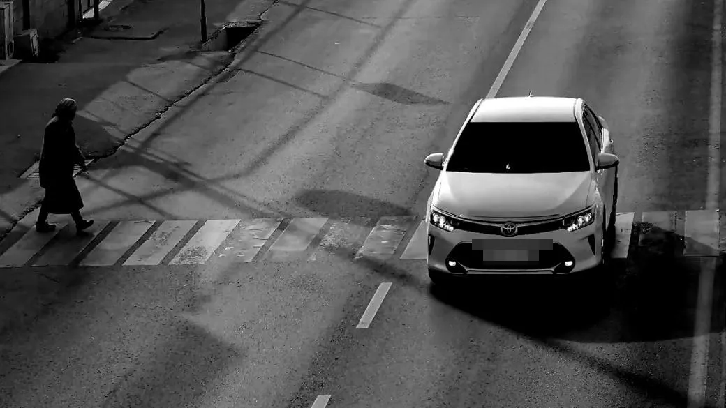 Monochrome LPR camera view of a sedan stopped in a crosswalk while a pedestrian crosses to its left