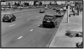 Monochrome LPR camera view of a multi-lane road with a pickup truck and other vehicles stopped near the curb