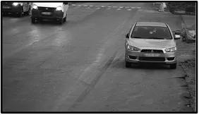 Monochrome nighttime LPR camera view of a sedan facing the camera while stopped on the roadway