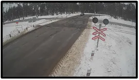 TL camera view of a snowy road approaching a railway crossing with a crossbuck signal sign visible ahead