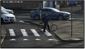 Exit LPR camera view of a pedestrian with a bicycle crossing a marked crosswalk near the intersection exit, with vehicles waiting nearby