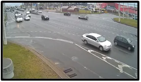 OV camera wide shot of several vehicles crossing an intersection curve with a roundabout-style road layout